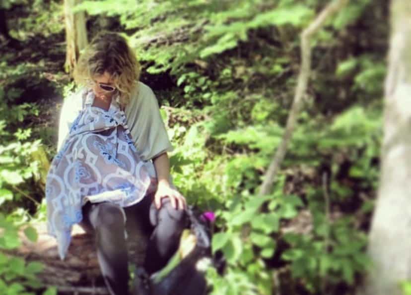 Mother breastfeeding baby under a nursing cover in the woods