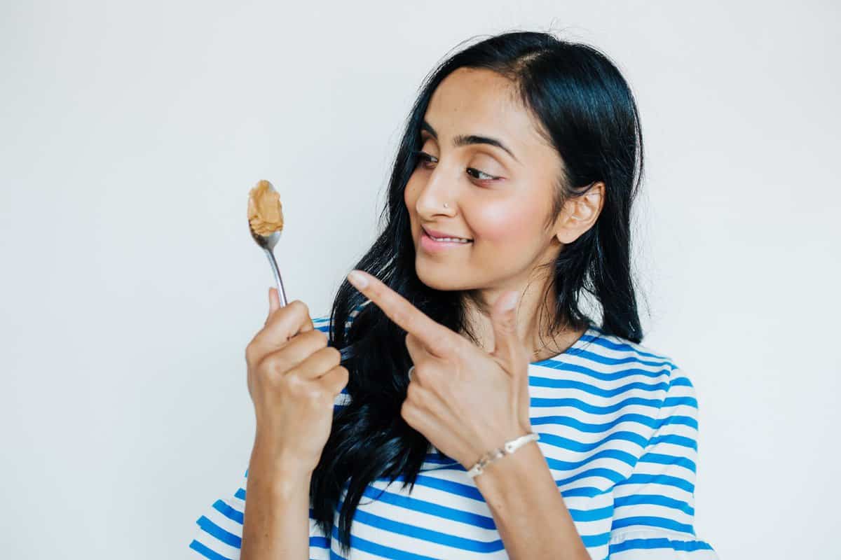 Women with long dark hair holding and pointing at a spoonful of peanut butter