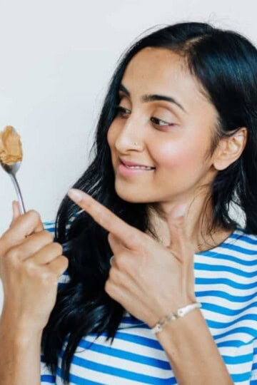 Woman with long dark hair holding and pointing at a spoonful of peanut butter