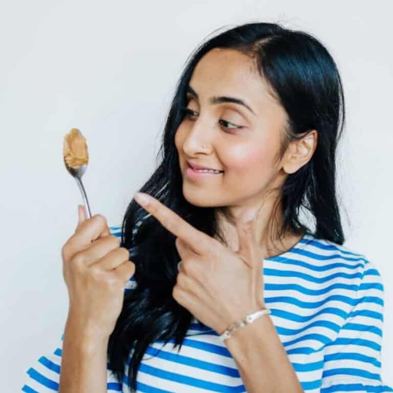 Woman with long dark hair holding and pointing at a spoonful of peanut butter