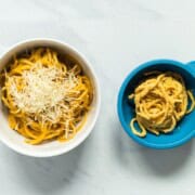 A side by side image of a bowl of creamy pumpkin spaghetti for the family and a bowl with slight adaptations for baby