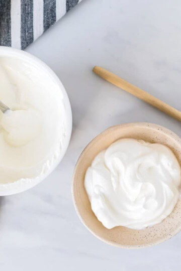 An open tub of plain yogurt beside a bowl of yogurt.