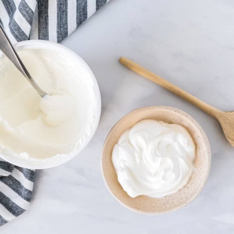 An open tub of plain yogurt beside a bowl of yogurt.