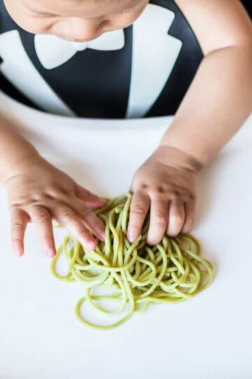 baby in highchair with spaghetti noodles on tray