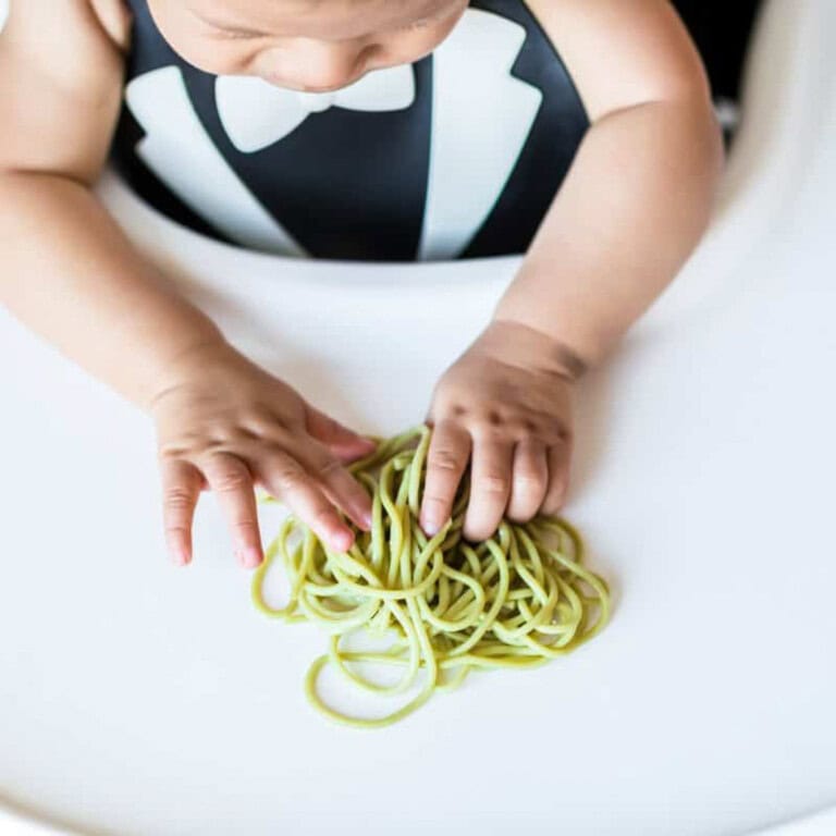 baby in highchair with spaghetti noodles on tray