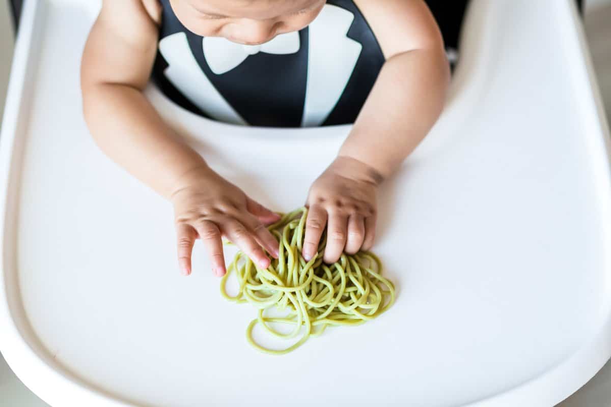 baby in highchair with spaghetti noodles on tray