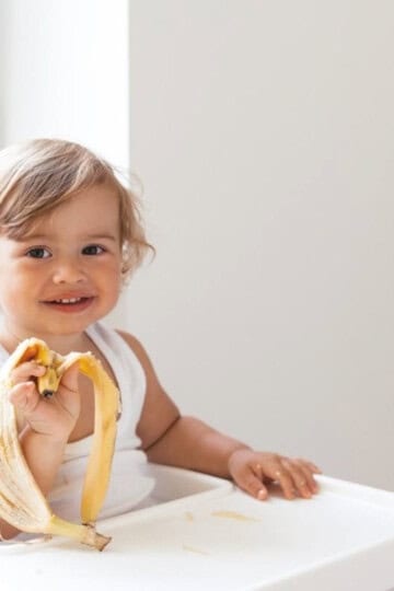 Young toddler girl sitting in high chair holding a banana peel