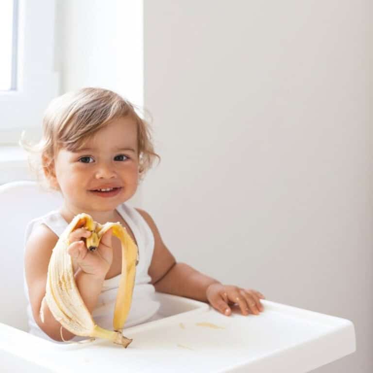 Young toddler girl sitting in high chair holding a banana peel