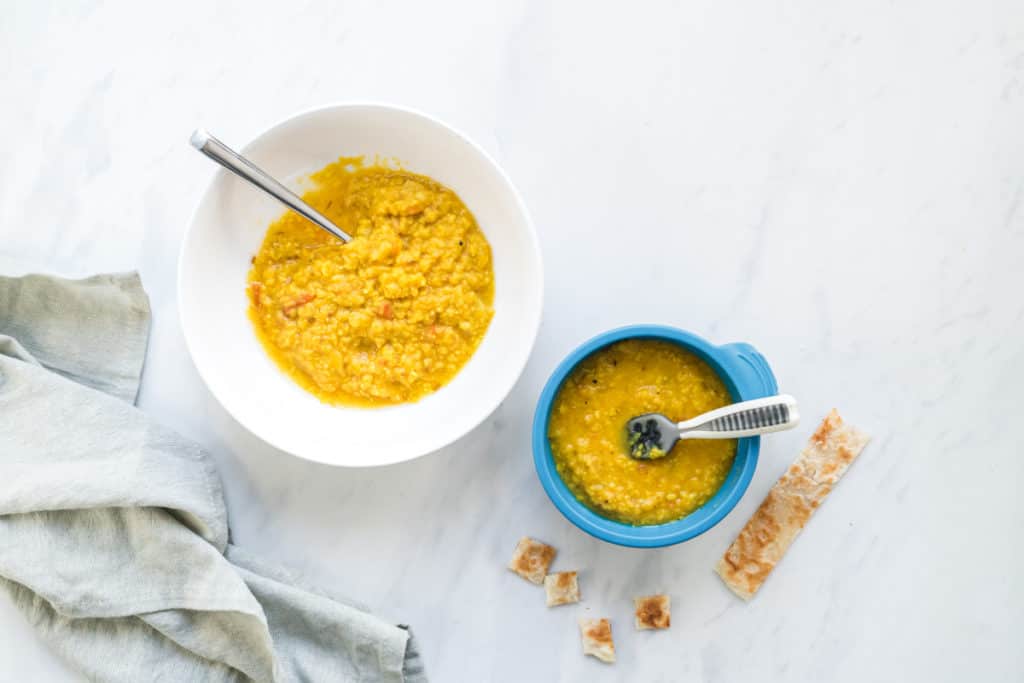 A side by side image of moong dal with the left bowl being suitable for the whole family and the right bowl being just right for baby. Paratha on side for dipping.