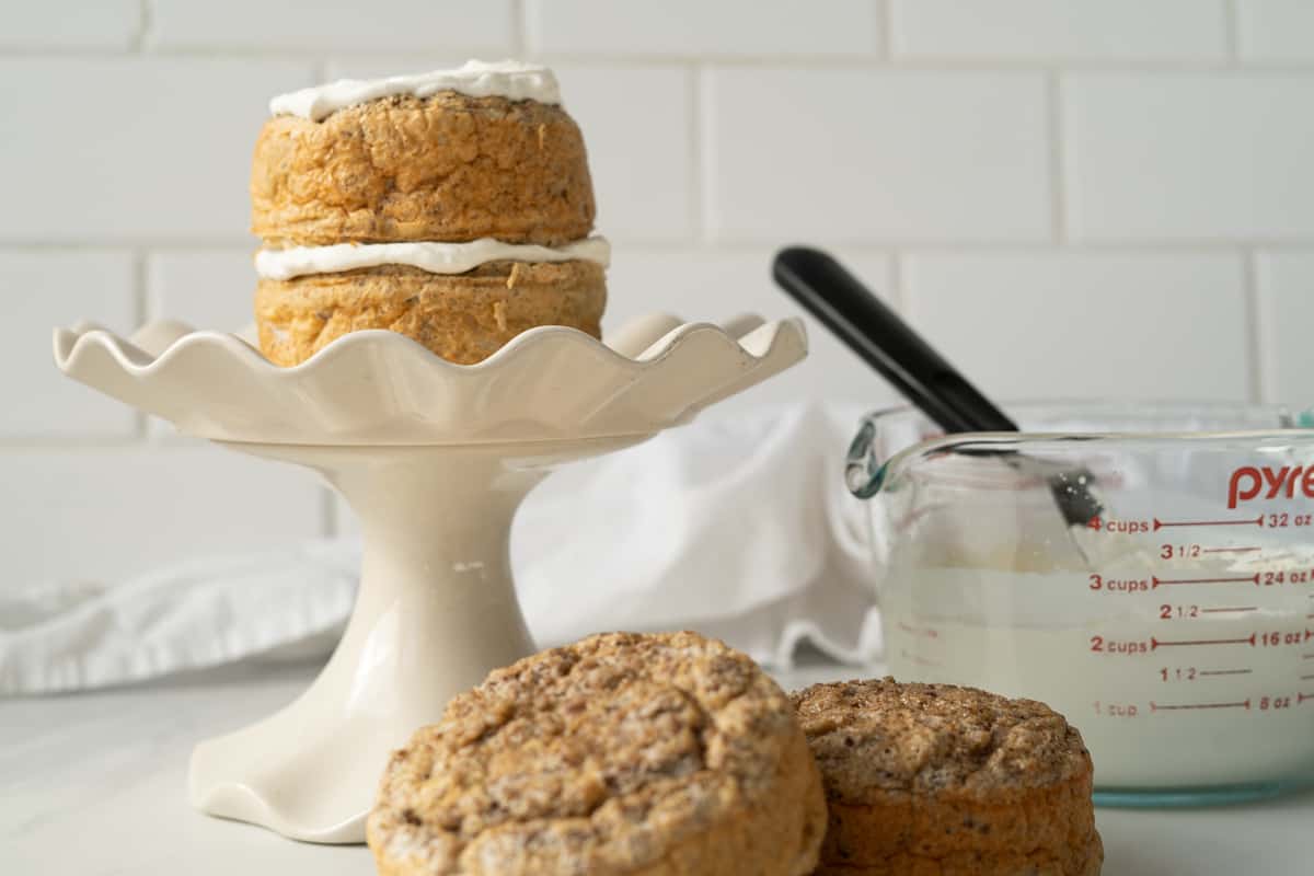 Two layers of a baby smash cake on a cake plate with the whipped cream frosting and other layers on the side ready to be added to the top.