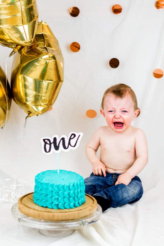 One year old boy crying in front of a smash cake