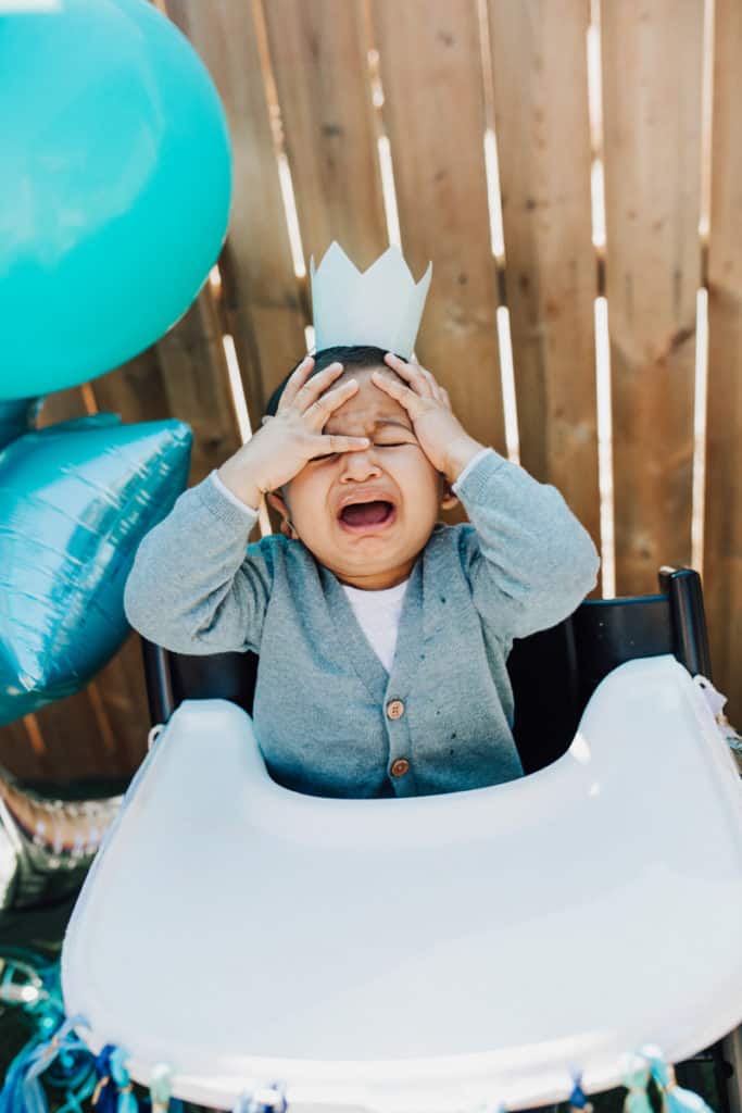 One year old crying at his birthday party wearing a crown