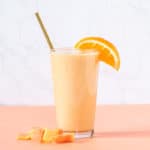 glass of papaya banana smoothie with an orange slice and pieces of papaya surrounding it