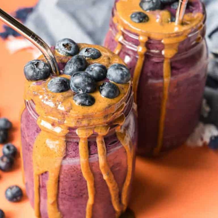 two mason jars with blueberry baby smoothies with almond butter drizzled on the side and loose blueberries surrounding the scene