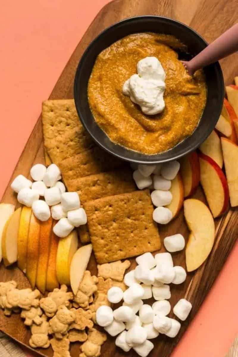 pumpkin pie pudding on a charcuterie style board with sliced pear, apples, mini marshmallows and graham crackers. 