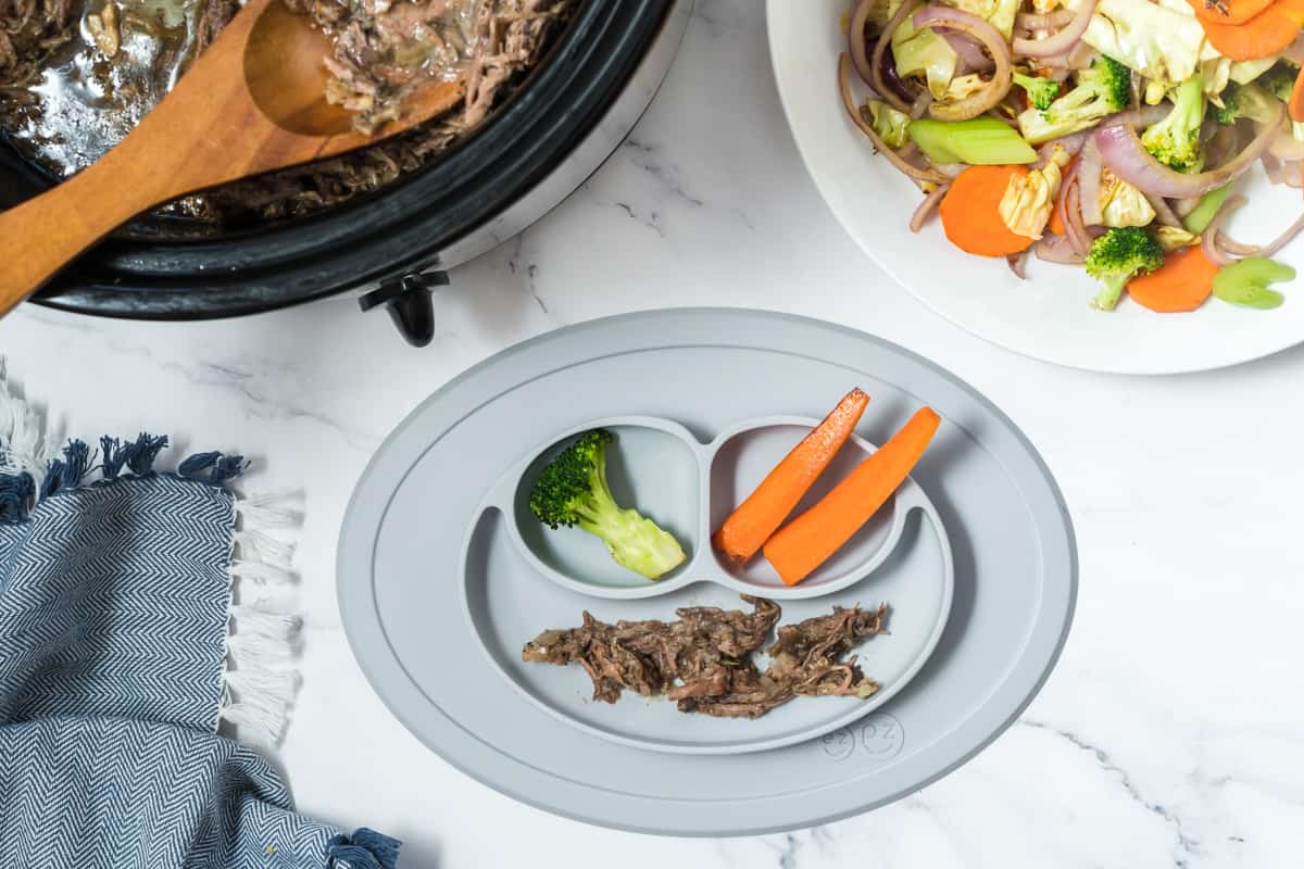a divided baby plate with shredded beef, steamed carrots and steamed broccoli