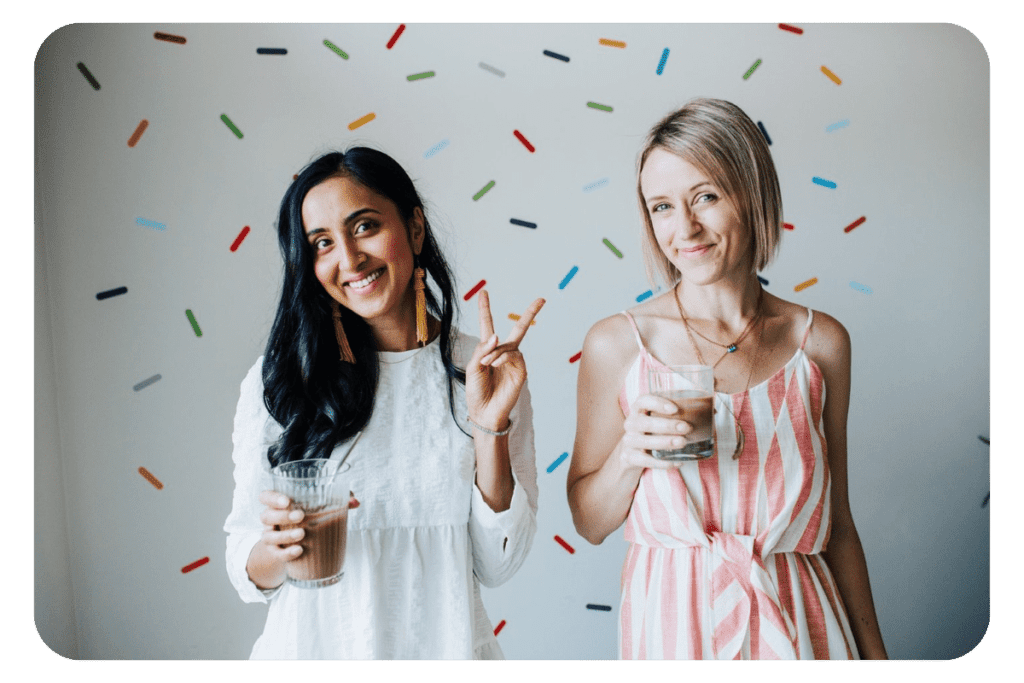 Jess and Nita holding iced coffees in front of a sprinkles background