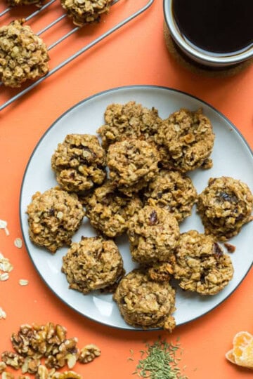 a plate of lactation cookies alongside a cup of coffee and a hand reaching for one cookie.