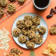 a plate of lactation cookies alongside a cup of coffee and a hand reaching for one cookie.