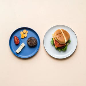 blended burgers: on the left is a deconstructed version for a 9 month old baby that includes the bean-beef burger, a toast strip, a wedge of tomato, and cheese slices cut into finger foods. On the right is a full burger for the parent.