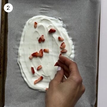Sprinkling finely chopped fruit onto yogurt to make yogurt bark for babies.