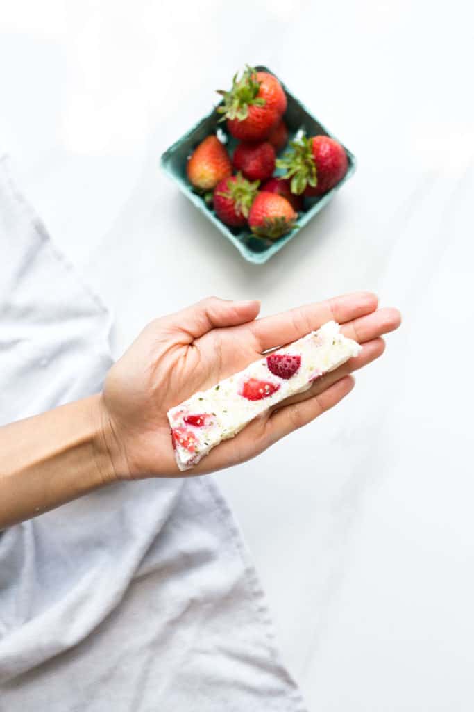 A hand holding a piece of strawberry frozen yogurt bark.