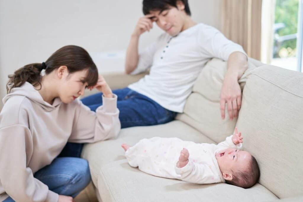 frustrated parents looking at their crying baby lying on a couch