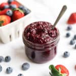 a jar of berry chia sauce surrounded by fresh strawberries and blueberries