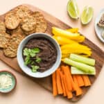 A bowl of kid-friendly black bean dip on a snack board with fresh veggies and crackers.