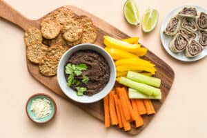 A bowl of kid-friendly black bean dip on a snack board with fresh veggies and crackers.