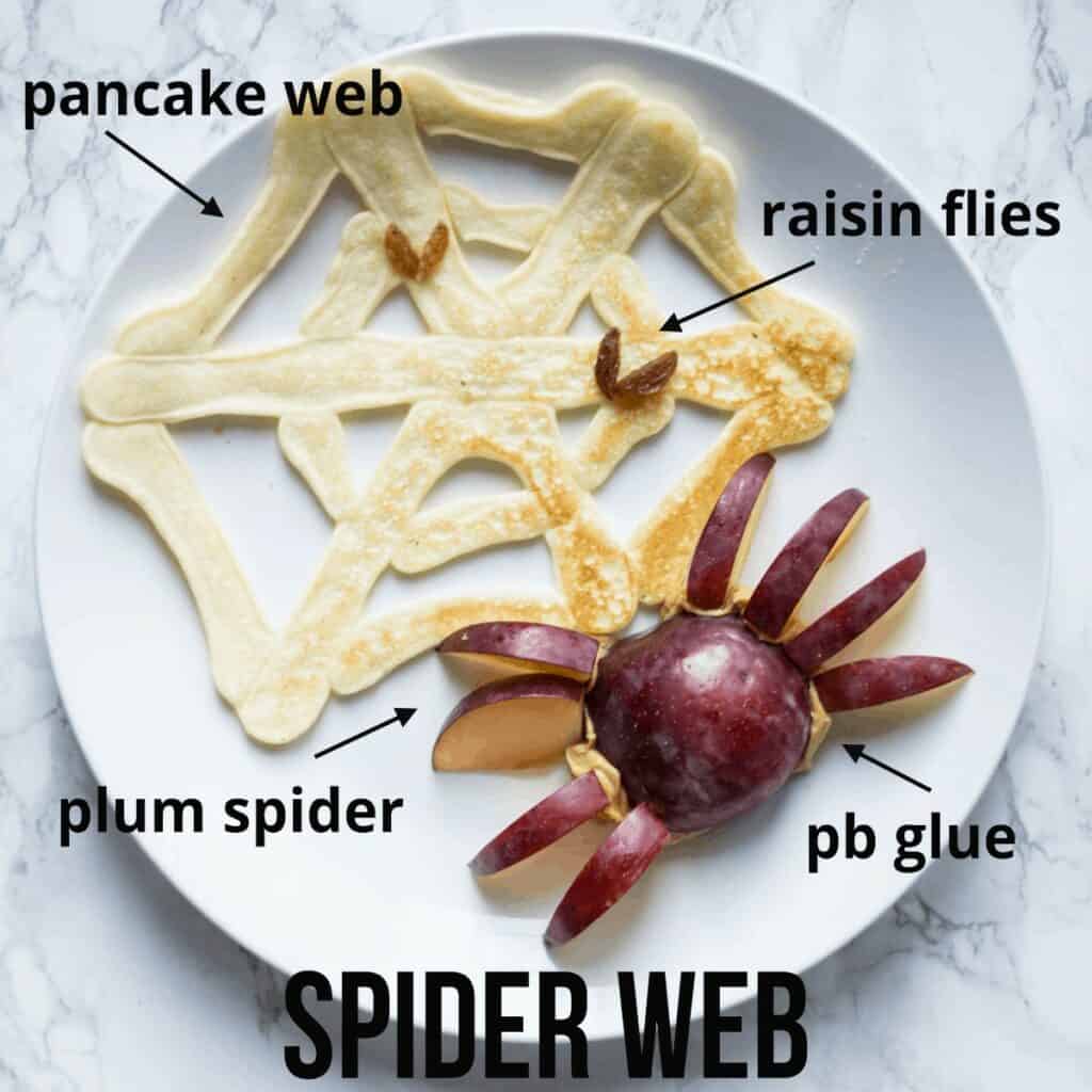 a pancake shaped as a spider web with a plum cut into the shape of a spider