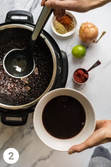black beans that are cooked in an electric pressure cooker with a hand holding a ladle of black bean excess liquid