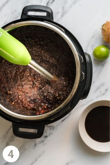 black bean dip being pureed in a large pot with a hand holding an immersion blender