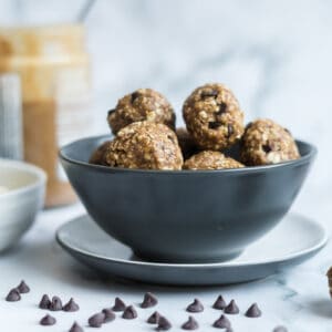 bowl of toddler oat balls surrounded by mini chocolate chips, bowls of ingredients, and a jar of almond butter.