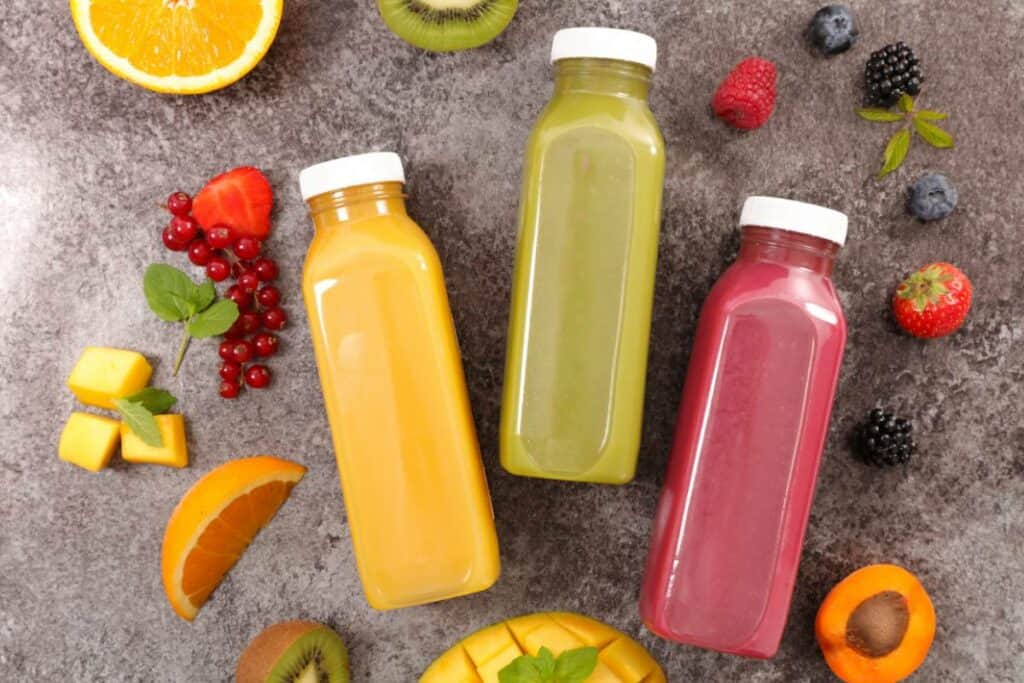 flatlay image of three bottles of juice: orange, kiwi, and berry