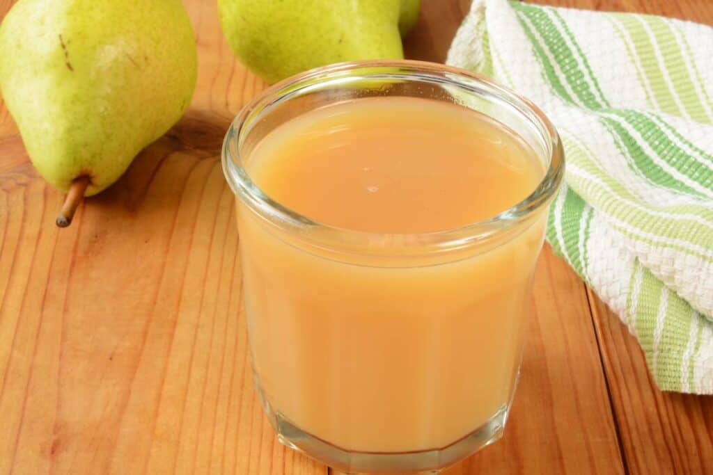A glass of pear juice with a couple of pears in the background.