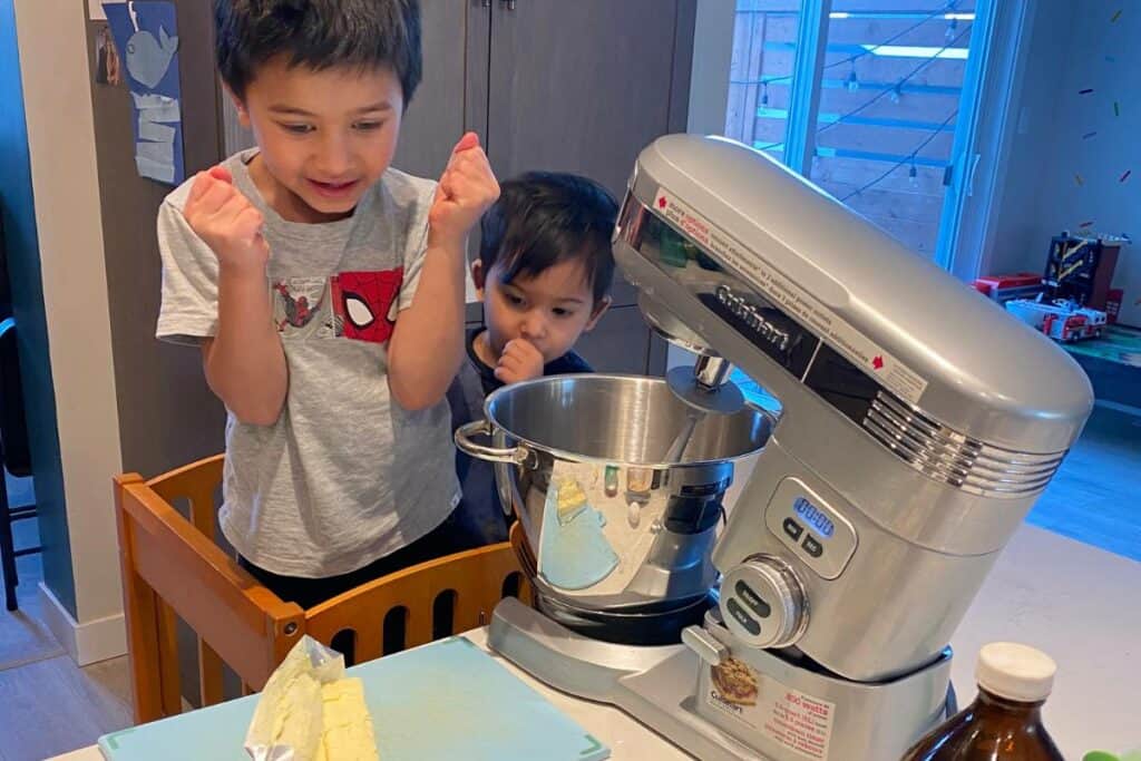 two boys in a learning tower excited to help make cookies using a stand mixer