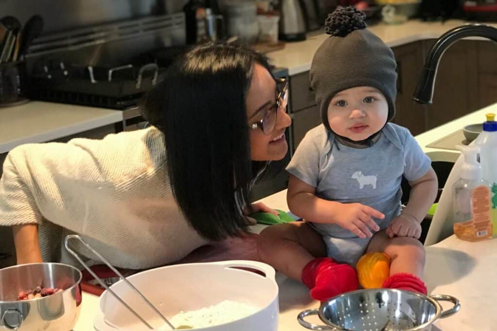 Baby sitting on a counter, supported by his mom while she takes a break from meal prep.