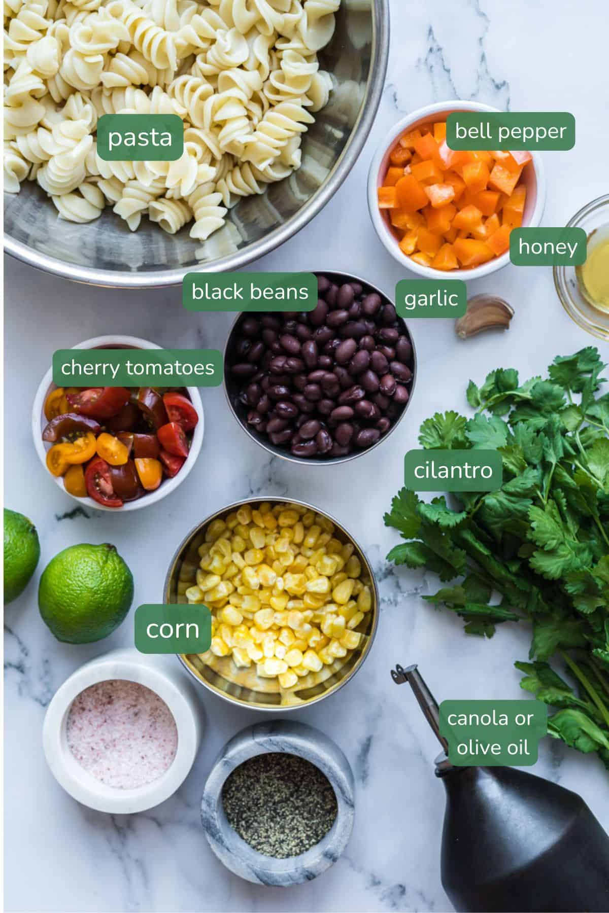 Flat lay of ingredients for the south west black bean pasta salad. Clockwise: cooked pasta, diced bell pepper, honey, garlic, cilantro, canola or olive oil, salt, pepper, corn, limes. cherry tomatoes and black beans.