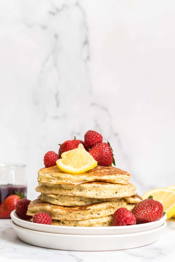 A tall stack of fluffy lemon ricotta pancakes with poppyseeds.
