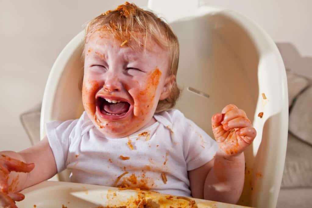 baby, messy from eating spaghetti, crying in high chair