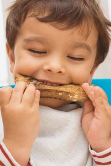 toddler with brown hair biting into a sandwich