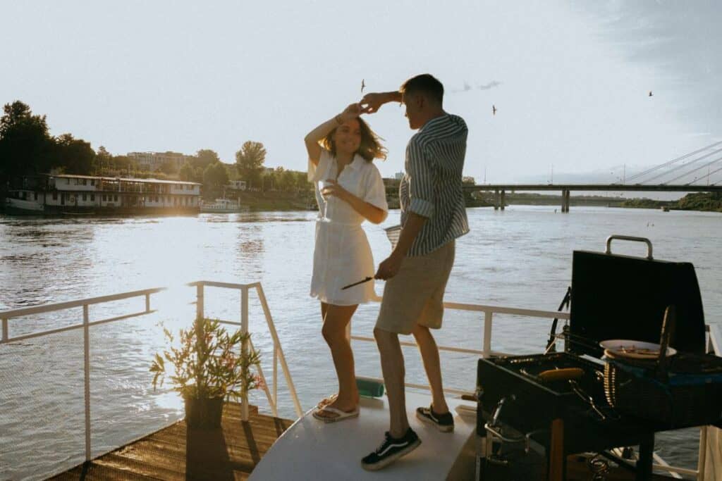 a couple dancing on a dock beside a bbq