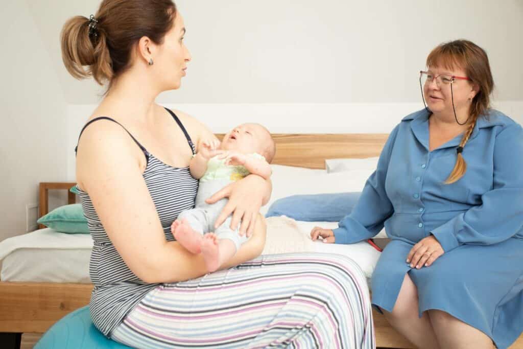 A lactation counselor talking with a mother on a hospital bed, holding a newborn baby