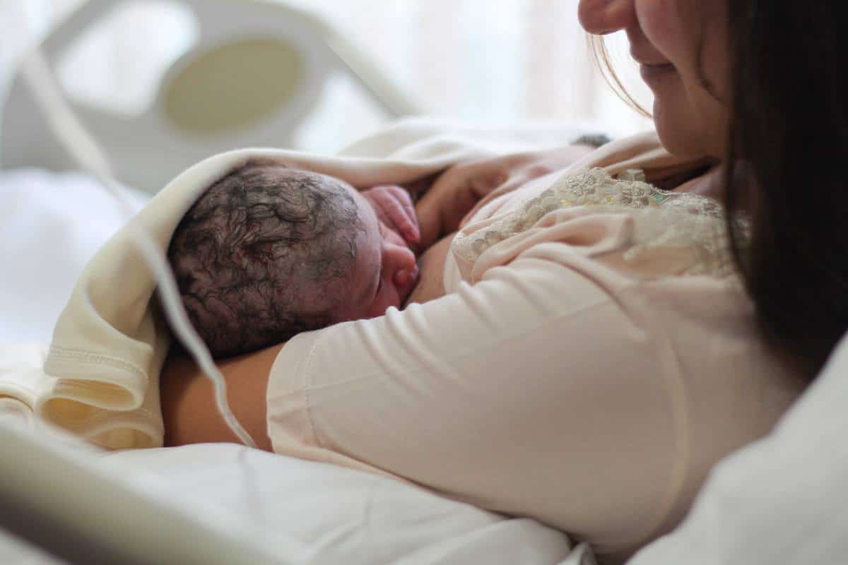 A mother in a hospital bed breastfeeding a newborn baby with vernix.