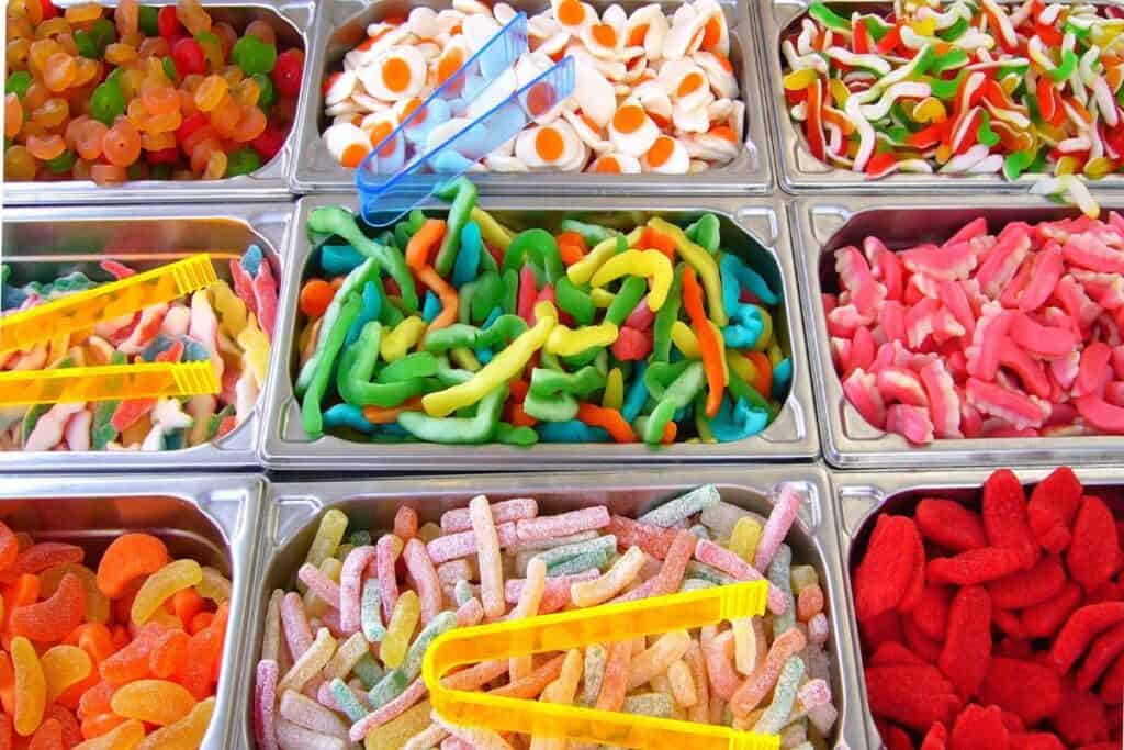 Several bins of gummy candy with tongs.