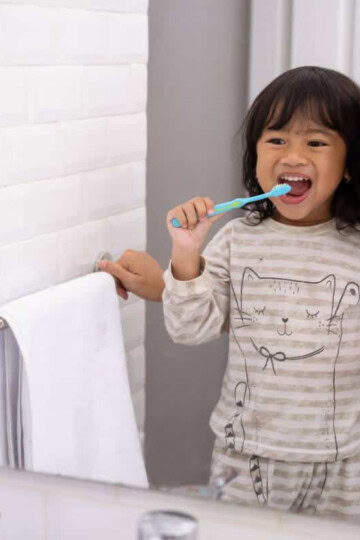 A toddler is brushing her teeth with the help of her mom.