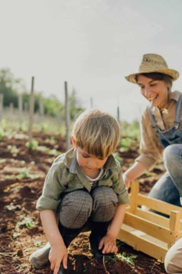 A farmer in overalls in helping a child plant seeds.