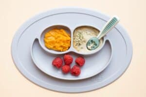 a divided baby plate with sweet potato puree, raspberries, and infant cereal topped with hemp hearts