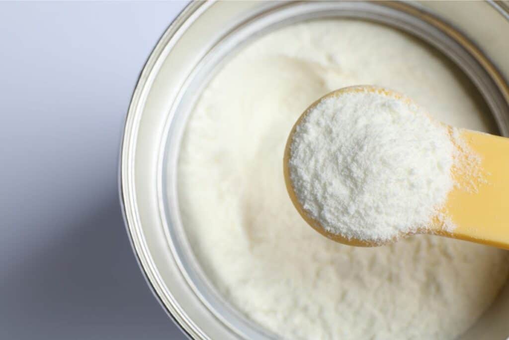 A closeup image of a scoop of powdered infant formula being scooped out of a can of formula